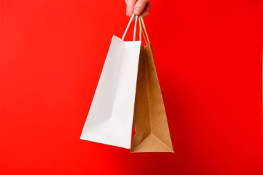 Kırmızı arka planda iki alışveriş çantası tutan kadın. Beyaz ve kahverengi el işi boş kağıt torbaları. Kara Cuma indirimi, indirim, alışveriş ve ekoloji konsepti