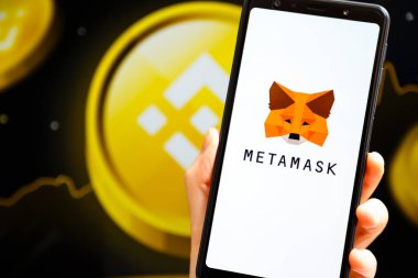 Ukrayna, Odessa - 9 Ekim 2021: MetaMaske uygulaması arka planda MetaMaske ve Binance logosu ile akıllı telefon ekranında çalışan el ele tutuşma uygulaması. MetaMaske Binance Akıllı Zincir kavramına bağlanıyor