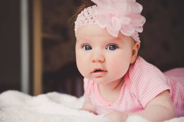 Pembe elbiseli, beyaz bir yatakta uzanıp kameraya bakan 3 aylık tatlı bir bebek. Kocaman açık gözler. Yatakta bebek şekerlemesi. Doğumdan kısa bir süre sonra sağlıklı küçük bir çocuk