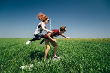 ODESSA, UKRAINE - 20 Mayıs 2015: Şirin genç hippi çift yeşil alanda sörf tahtası ile dalga geçiyor, kız erkeğin üzerine atlıyor, açık havada eğlenceli bir portre.