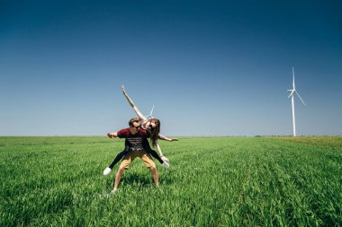 ODESSA, UKRAINE - 20 Mayıs 2015: Şirin genç hippi çift yeşil alanda sörf tahtası ile dalga geçiyor, kız erkeğin üzerine atlıyor, açık havada eğlenceli bir portre.