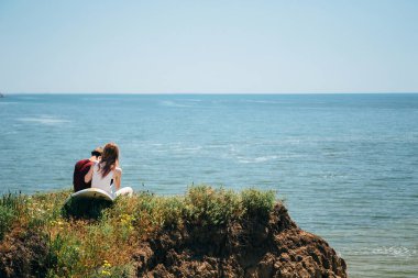 ODESSA, UKRAINE - 20 Mayıs 2015: Tepede denize bakan sörf tahtası olan sevimli genç bir çift hippi. Arka plan.