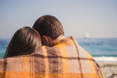 Genç ve mutlu bir çift sahilde oturup okyanus kenarında sarılıyor, mutlu bir yaşam tarzı aile kavramı..