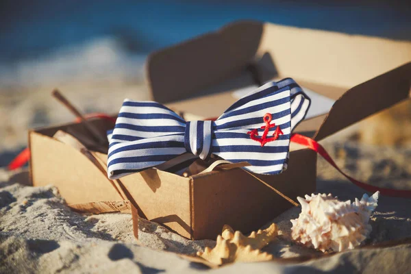 Stylish bow tie in the craft box at the sand. Men's and women's accessories on the sandy beach background.