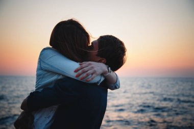 Close up of young couple hugging at sunrise beach background, summer time.