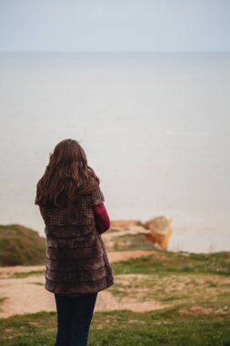 Young woman looking at the sea standing alone at the coast outdoors.