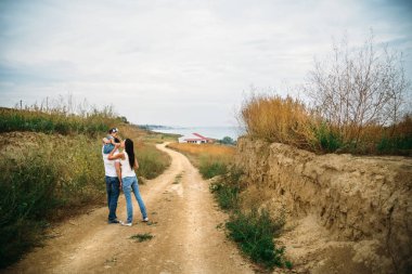 Beyaz tişörtlü, kot pantolonlu, el ele tutuşan, öpüşen, arka planda gezen küçük bir kızı olan mutlu bir aile..