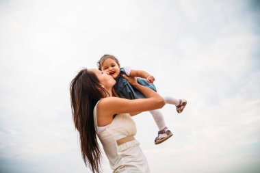 Küçük kızıyla oynayan mutlu bir genç anne. Havaya fırlatıyor, arka planda kalıyor..