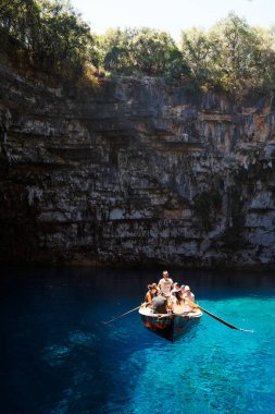 Melissani Cave, Cephalonia island, Greece - July, 14 2019: A small boat with group of tourists in the middle of Melissani Lake with fantastic blue sea water