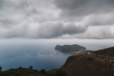 Asos köyü ve Assos yarımadasında kötü hava koşulları, sağanak yağış ve düşük kara bulutlar ve denizde görülebilir akıntılarla bir yol manzarası. Sefalonya, Yunanistan