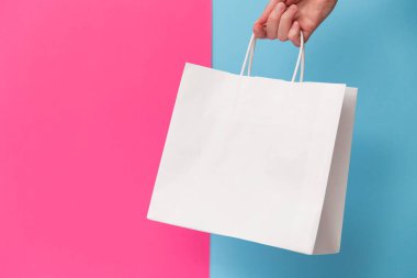 Female hand holding white blank shopping bag isolated on pink and blue background. Black friday sale, discount, recycling, shopping and ecology concept