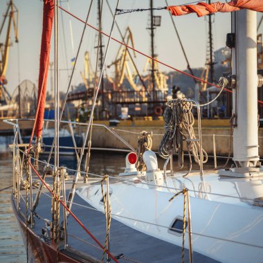 Sail yacht standing moored in the sea port, sailboat harbor. Forward, sail and nautical ropes yacht details. Modern water transport. Yachting, marine background.