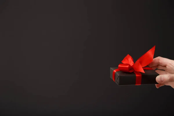 Woman\'s hand holding black gift box with red bow over black background. Black friday sale, Christmas sale, discount concept. Valentine\'s day. Father\'s day