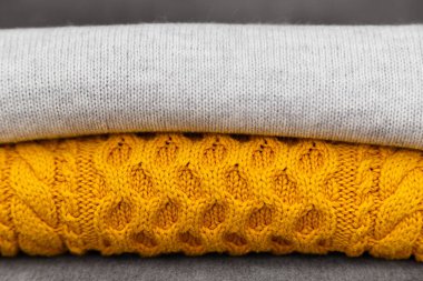 Knitted pullovers close up in trendy grey and yellow colors. Colors of the 2021 year. Stack of cozy knitted sweaters, warm concept.