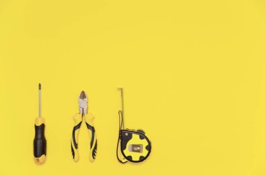 A flatlay with a set of bench tools, screwdriver, cutting pliers and tape measure on yellow Illuminating background. Colors of the 2021 year