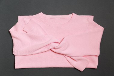 Knitted pullover in trendy light pink color on a dark gray background in flay lay style.