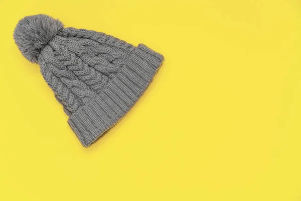 Knitted gray hat with pompon on a yellow 13-0647 Illuminating background. Colors of the 2021 year. Cozy knitted accessory in trendy colors, warm concept.