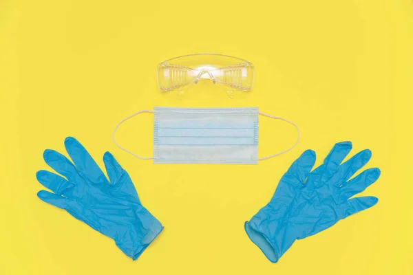 Coronavirus personal protective equipment. Medical nitrile gloves, protective glasses and mask on the yellow Illuminating background, color of the 2021 year. PPE concept in 2021 color trends