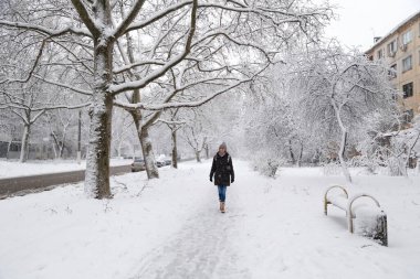 Young woman walking alone at empty snow-covered winter street. Snowy winter