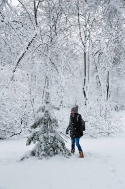 Young smiling woman standing near to a small fir tree in a snow-covered winter forest. Snowy winter.