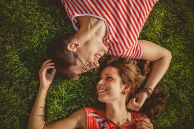 Young loving couple lying together head to head on a grass at summer. Both in red clothes and holding hands. Overhead top view.