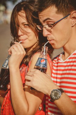 ODESSA, UKRAINE - OCTOBER 15, 2014: Close up of young happy teenage couple outdoors drinking cold Pepsi from glass bottles with straw.