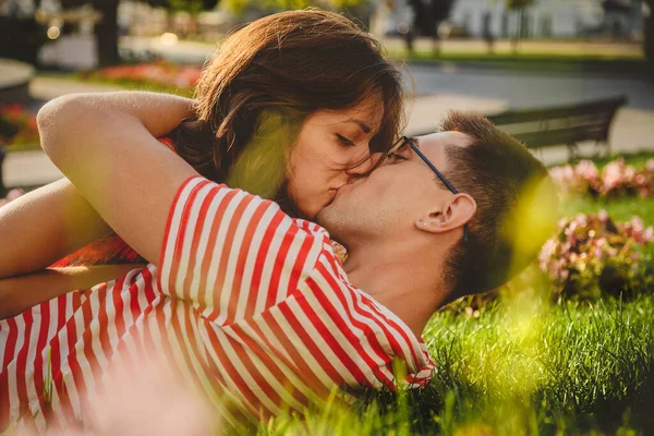 Lovely couple lying on green grass in park, kissing and spending time together.