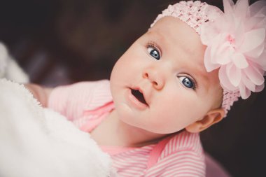 Close-up portrait of cute 3 months old smiling baby girl in pink lying down on a white bed at home. Big open eyes. Healthy little kid shortly after birth