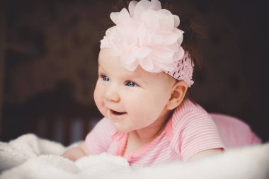 Close-up portrait of cute 3 months old smiling baby girl in pink lying down on a white bed at home. Big open eyes. Healthy little kid shortly after birth