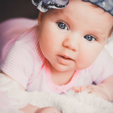 Close-up portrait of cute smiling baby girl in pink lying down on a white bed. Big open eyes