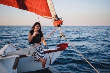Young pretty woman in black shirt and striped skirt with a glass at luxury yacht in sea, sunset.