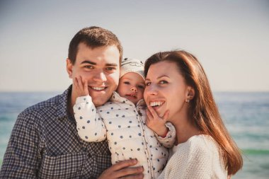 Genç ve mutlu bir ailenin ortasında küçük bir çocuk, okyanus kenarında birlikte eğleniyorlar, mutlu bir yaşam tarzı aile kavramı..