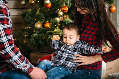 Christmas family portrait of young happy smiling parents playing with small child near the christmas tree. Winter holiday Xmas and New Year concept.