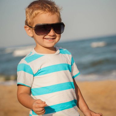 Happy stylish boy in sunglasses and striped t-shirt enjoying life on summer beach.