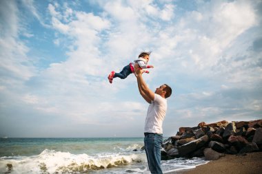 Happy young father playing with a small daughter, throwing in the air, outdoors background.