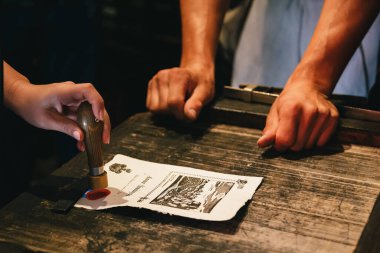 Bled, Slovenia - September, 8 2018: Woman's hands making souvenir, personal stamp of melted red sealing wax at old-style picture post card. Souvenir shop at Bled Castle on Lake Bled, Slovenia.