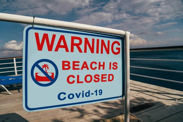 Beach is closed due to Covid-19 warning sign located at an entrance to a beach. Social media campaign for coronavirus prevention. Summer is cancelled, shutdown concept.