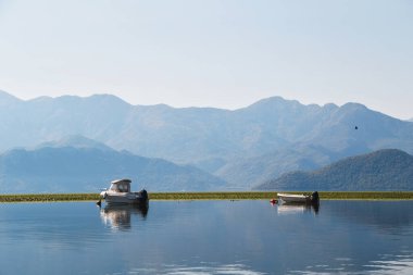 A beautiful view at lonely boats in the middle of the lake Skadar with blue mountain view at background in Montenegro National Park. The largest lake in Southern Europe