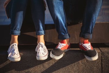 Odessa, Ukraine - October, 14 2014: Top close up view of young couple legs in sneakers and jeans sitting together outside