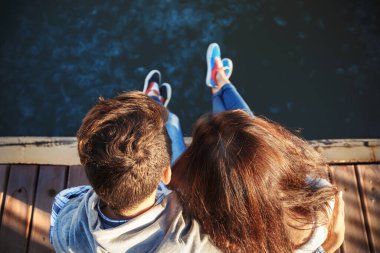 Top close up view of young couple sitting on pier near to the sea full of jellyfish