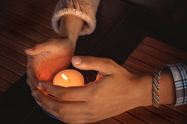 Close up of couple's hands cupped around a burning candle. Hands of young man and woman that protect the flame of a candle. Love story concept.