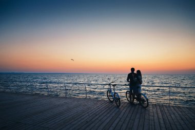 Plajda sarılıp tahta güvertede güneşin doğuşunu izleyen genç hippi aşıklar..