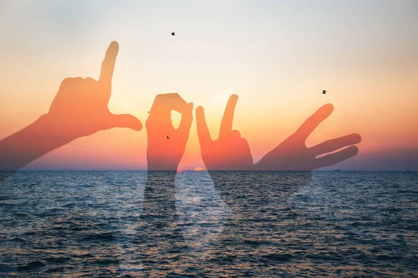 Word love silhouette of two young people making love shape of hands at the beach at sunrise sky summer time, seashore summer beach at yellow blue evening horizon sea, sunset background.
