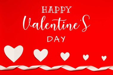Happy Valentine's day card. White paper hearts and white ribbon on red background in flat lay style. Valentines day concept.
