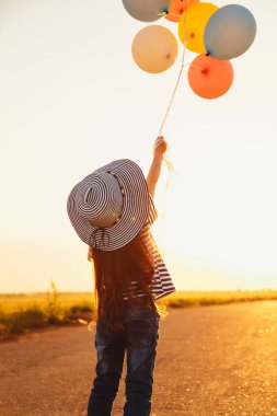 Little girl at road playing with colorful balloons at sunset.