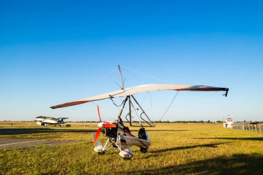 Motor hang glider standing on green grass at aerodrome, bright summer day.