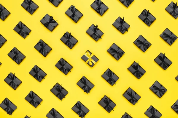 Pattern with black gift boxes with black ribbons on bright rich yellow background. Black Friday sale flat lay, top view. Discount, advertising and sale concept. Creative minimalist design