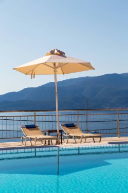 Boş şezlonglar ve güzel deniz manzaralı şemsiyeli lüks yüzme havuzu..