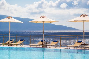 Luxury swimming pool with empty deck chairs and umbrellas at the resort with beautiful sea view.