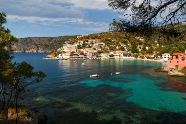 A view at green, blue bay, sea-front street of Asos village, greek colorful houses and turquoise Ionian Sea water. Summer scenery of famous travel destination in Europe.